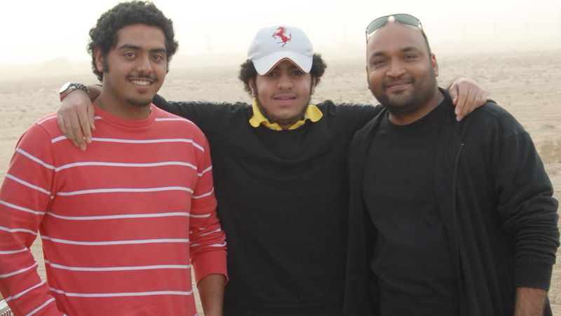 Three men posing together on a beach